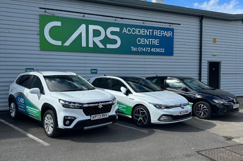 Three branded cars parked outside CARS Accident Repair Centre, a grey building with a green and white sign.
