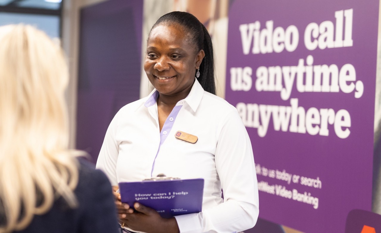 The image shows a NatWest Group colleague in a branch talking to a customer