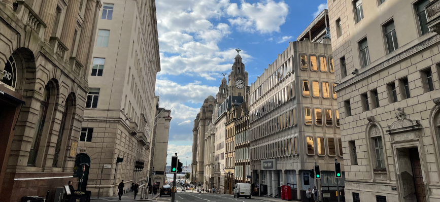 Street view in Liverpool featuring historic buildings and the Royal Liver Building with its clock tower in the background.