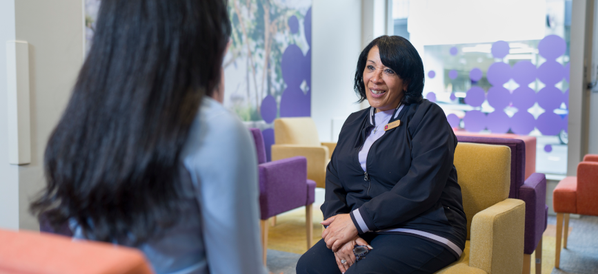 NatWest colleague speaking with a customer in the Kensington branch lounge area, featuring colourful chairs and large windows.