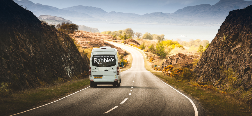 A Rabbies tour bus driving down a long road with hills on each side