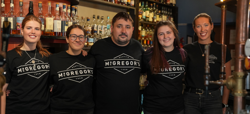 A group photo of MacGregor’s Pub staff smiling behind a bar