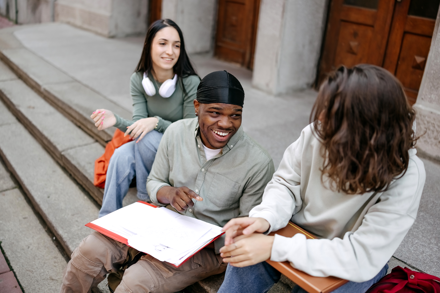 This image shows a group of young people together sat on some steps. The male in the middle has a notepad open.