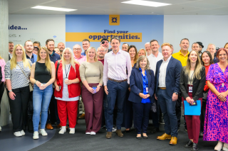NatWest Group CEO Paul Thwaite stands with a group of entrepreneurs at the Royal Bank of Scotland Accelerator Hub in Glasgow. The group is posing for a photo in front of a wall with the text "Find your opportunities." The individuals are dressed in business casual attire, and the setting appears to be an office or conference room.