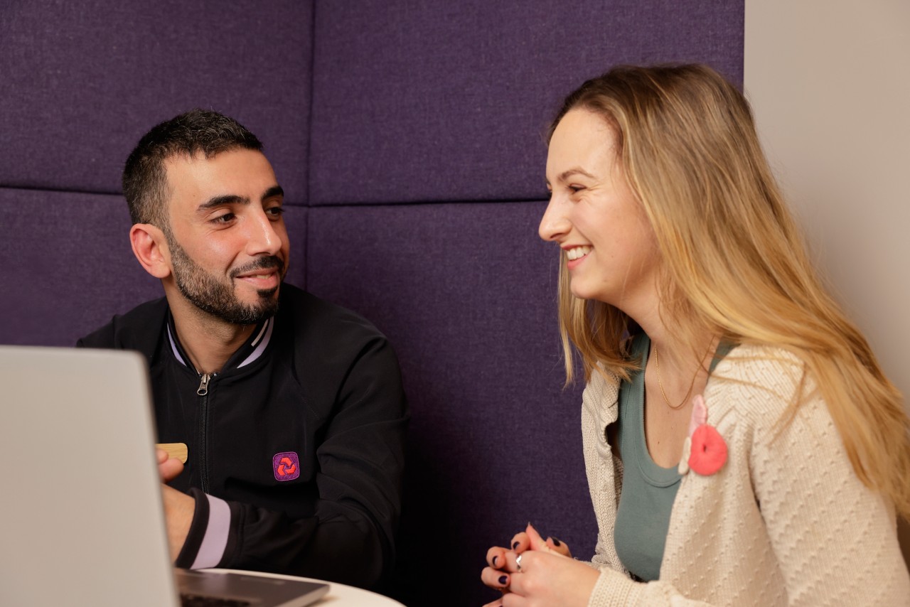 This image shows a NatWest Group colleague sat at a desk with a customer. They are looking at a laptop. 