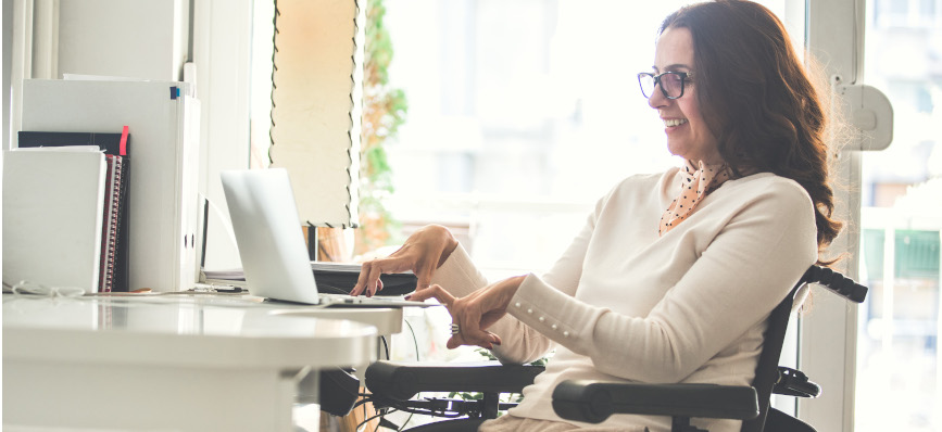 Side view of a woman in a motorised wheelchair working on a laptop in the office.