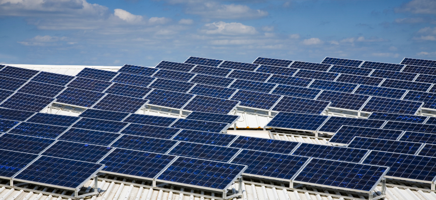 A worker using a laptop on a roof covered with solar panels