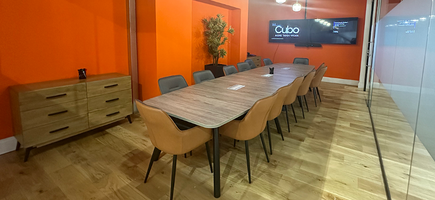 Image of a corporate meeting room with a long wooden table with chairs and an orange walls – a tv displays the Cubo logo