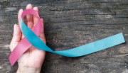 A hand cradles a pink and blue awareness ribbon