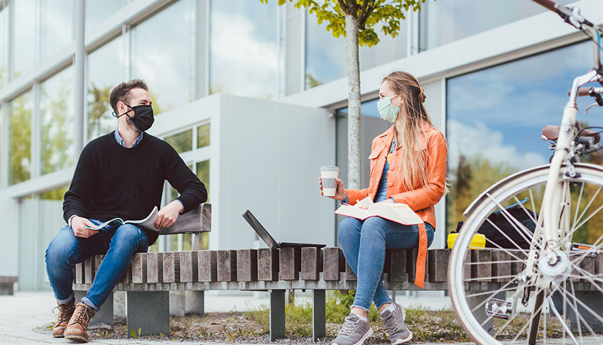 Two people wearing masks chatting on a bench