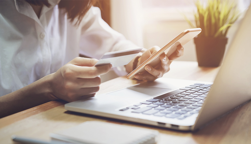 Woman holding credit card and smartphone sitting in front of laptop