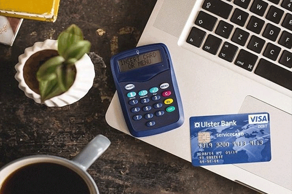 Bank card, card reader, coffee cup and computer on a tabke