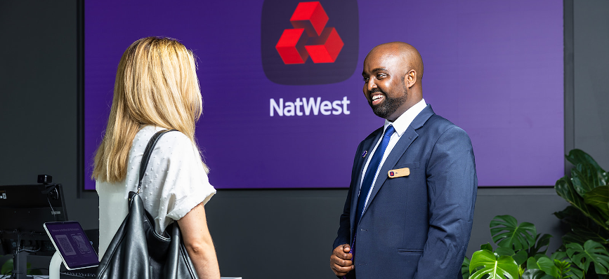 colleague in suit greeting customer in NatWest building – NatWest logo in background