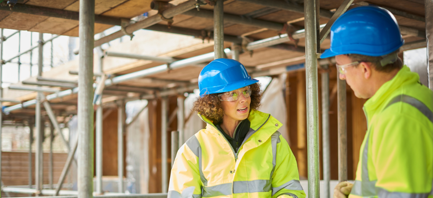 Man and woman on a building site with hi-vis jackets and blue helmets