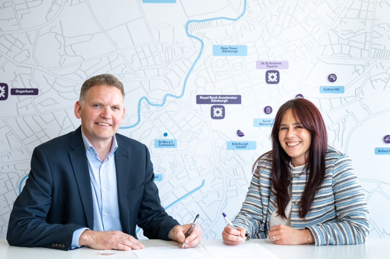 This image shows a female Royal Bank of Scotland colleague signing the bank’s partnership agreement alongside a male colleague from the University of Edinburgh. They are sat at a table. 